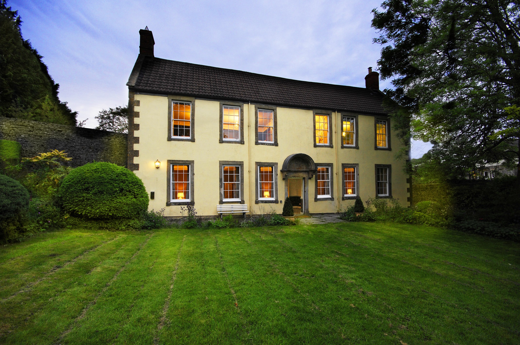 A stone farmhouse at dusk with its windows lit